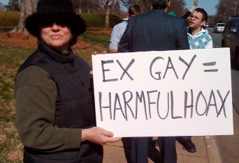 Woman holding sign that says "Ex-gay = harmful hoax"