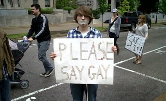 Student holding "please say gay" sign.
