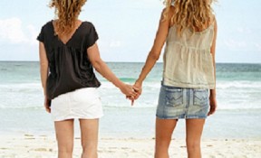 Two women holding hands at beach, rear view